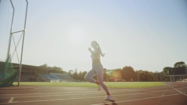 Beautiful Fitness Woman in Light Blue Athletic Top and Leggings is Starting a Sprint Run in an Outdoor Stadium. She is Running on a Warm Summer Day. Athlete Doing Her Sports Practice. Tracking Shot.