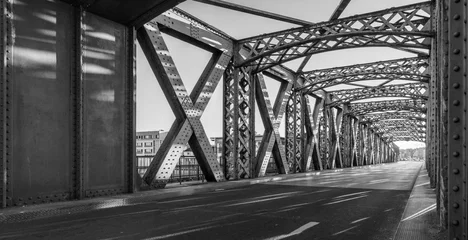 Foto op Plexiglas Zwart-wit asfaltweg onder de staalconstructie van een brug in de stad op een zonnige dag. Avond stedelijke scène met de zonnestraal in de tunnel. Stadsleven, vervoer en verkeer concept. © sergiymolchenko