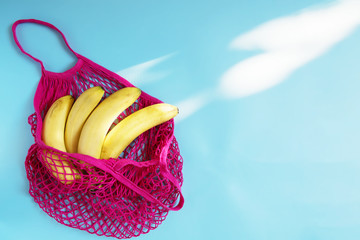 Organic banana in mesh string bag on pastel blue background. Flat lay, top view. Zero waste, plastic free concept. Healthy clean eating diet and detox