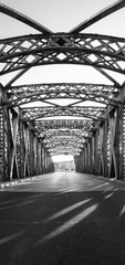 Black and white asphalt road under the steel construction of a bridge in the city on a sunny day. Evening urban scene with the sunbeam in the tunnel. City life, transport and traffic concept.