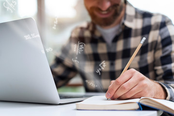 Close-up on a young man's hand while he is keeping mathematical notes in his notebook holding a...