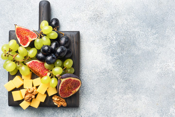 Cheese cubes, fresh fruit figs grapes Honey walnut on wooden chopping Board. Copy space.