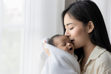 Obraz na płótnie Canvas Portrait of asian young mother kissing her cute newborn baby in white bed room. Wife and mother's day concept.