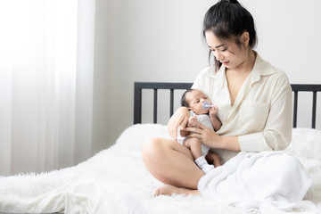 Portrait of Asian young mother with cute newborn baby sucking fake nipples and looking hers mother...
