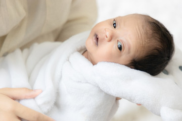 Young Asian mother hugging a cute newborn baby looking in white bedroom. Duty of the wife to raise children. Mother and child concept.