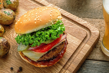 Hamburger with grilled vegetables and scallion served on a wooden board and a glass of beer on a tale. Top view, shot from above, close-up.
