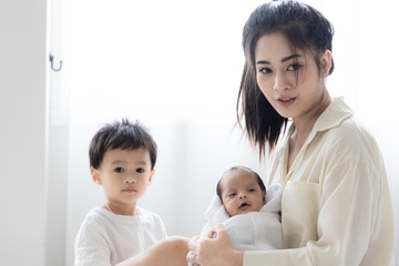 Asian young mother with cute newborn baby and the son in bed. Happy family and mother 's day concept.