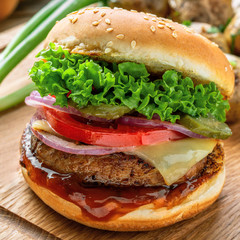 Cheeseburger made of meat burger, cheese, tomato, lettuce, onion and pickled cucumber with baked potato and broccoli. Close-up shot.