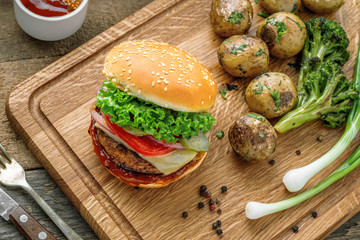 Cheeseburger made of meat burger, cheese, tomato, lettuce, onion and pickled cucumber with baked potato and broccoli. Top view, shot from above.