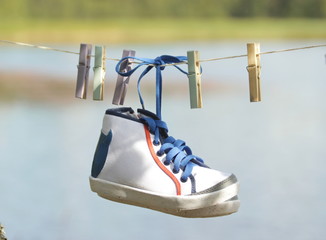 Pictures from a country holiday concept. Children's white sneakers with blue laces and colorful clothespins hanging on a clothesline. Blurred background of the lake.