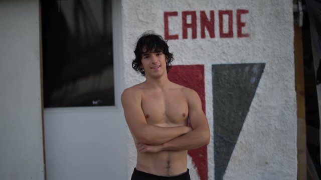 Portrait of handsome attractive shirtless athletic young man with arms crossed after canoeing training looking at camera by the sports club in summer. Cine lens.