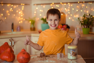 happy seven year old happy boy in the kitchen preparing gingerbread cookie and showing class. Waiting for Halloween