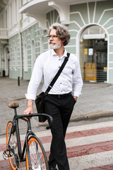 Obraz na płótnie Canvas Photo of brooding mature businessman walking with bicycle