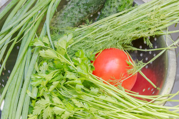 Tomatoes, cucumbers and greens in a metal colander