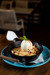 Traditional english crumble cake with apples and scoop of vanilla ice cream served in cast iron baking pan