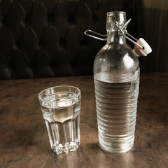 Bottle with open porcelain cork and glass full of water on the table. Toned image with copy space.