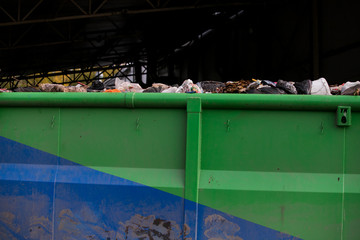 Naklejka premium A garbage container. A large black container filled with debris. Bags of garbage of different colors and a mountain rise above the container. There
