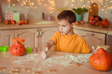 7 happy cute baby sitting at a table in the kitchen waiting for Halloween and preparing a gingerbread cookie