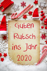 Fototapeta na wymiar Bright Vertical Paper With German Text Guten Rutsch 2020 Means Happy New Year. White Wooden Background With Snow. Flat Lay With Christmas Decoration, Like Candy Sticks, Sled, Santa Hat And Snowflakes