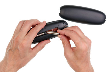 Elderly senior man inserts AAA size batteries into a oval shape cordless home telephone handset isolated