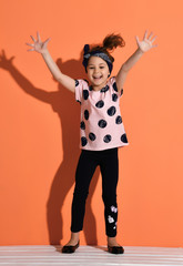 Laughing kid girl in is standing holding her hands up, jumping, dancing, having fun, showing ten