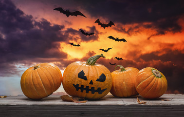 Ominous sunset with clouds and bats. Scary pumpkins on a wooden table. Halloween concept.
