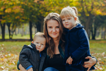Obraz na płótnie Canvas Beautiful young mother with daughter and son are walking in the autumn park. close-up portrait