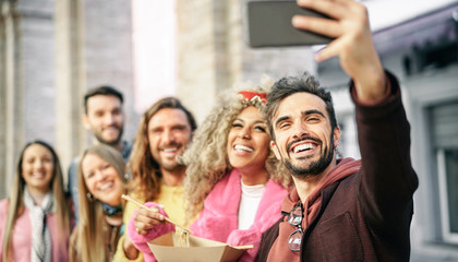 Group of multiracial friends eating Asian street food and taking selfie outdoor - Young trendy people having fun with new mobile smartphone apps while having a meal outside - Tech and social concept