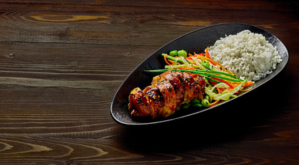 Teriyaki chicken with cucumber, ginger, cabbage and carrot salad, edamame soy beans and basmati rice in a black pottery dish.