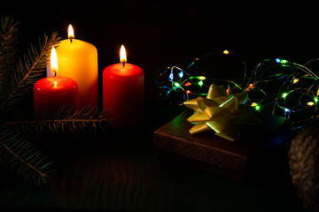 Christmas, New Year's still life with candles, spruce branch, gifts and a bowl with a garland on a dark background.