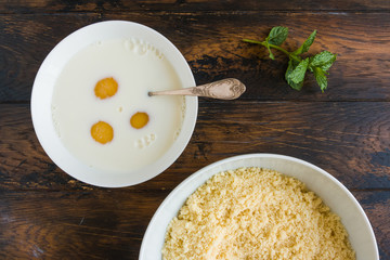 Dough making. Mixing eggs and milk in white bowl. Wooden rustic table, top view