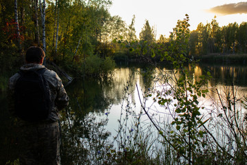 A fisherman on a forest lake fishes at sunset in the fall