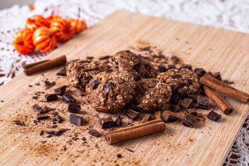 Chocolate cookies on wooden table with cinnamon sticks. Autumn style food photo with pumpkin.