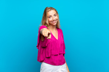 Blonde young woman over isolated blue background points finger at you with a confident expression