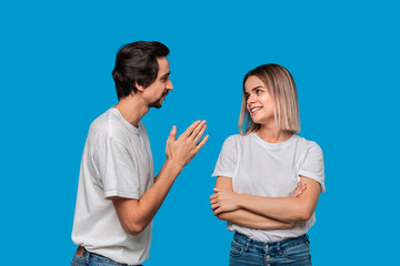 Brunet bearded man with mustaches in white t-shirt and blue jeans asking his girlfriend for forgiveness isolated over blue background. Concept of guilt.
