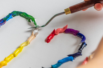 Bright squeezed oil paints on canvas. Girl draws with a palette knife. The process of creating a picture.