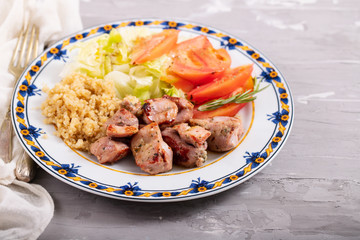 fried meat with quinoa and fresh salad on plate on ceramic background