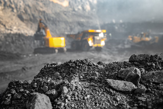 Coal open pit mine. In background blurred loading anthracite minerals excavator into large yellow truck