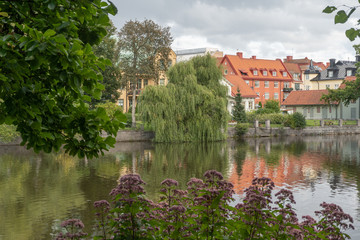 Fototapeta na wymiar Buildings and willow in town park. Reflections. Orebro town. Background or illustration. Travel photo.