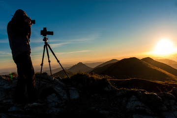 Photographer is taking pictures during sunrise on the top of the mountains
