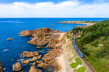 Obraz premium 青森県 深浦町にある行合崎付近の奇岩沿いを走行するリゾート列車を俯瞰撮影