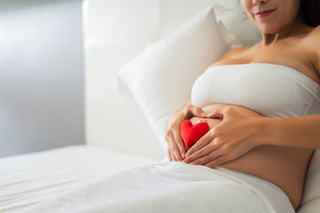 Pregnant woman holding her hands in a heart shape on her baby bump.