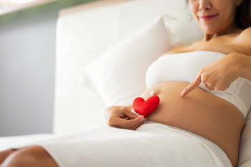 Pregnant woman holding her hands in a heart shape on her baby bump..