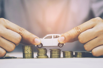 Business man and close up hand holding model of toy car white on over a lot money of stacked coins - insurance, loan and buying car finance concept. buy and installments down payment a car.