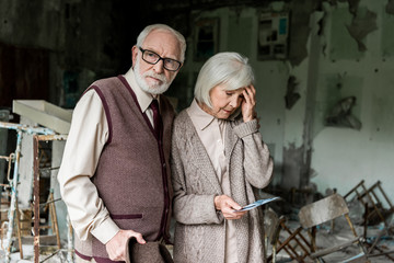 retired couple standing in abandoned school and holding photo