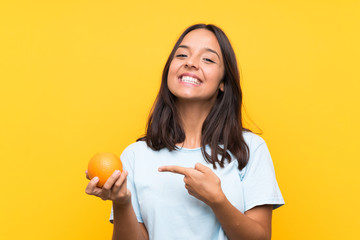 Young brunette woman holding an orange and pointing it