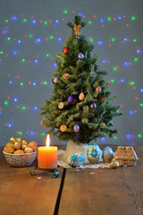 Christmas tree surrounded by the candles burning and eggs coloured on the table 