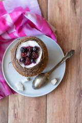 Berry dessert with yogurt in a cup of coconut on a wooden background. Blackberries, raspberries, blueberries, black currants.