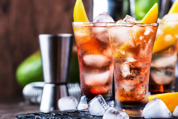 Alcoholic cocktail with mango, cranberries, lime, crushed ice and liquor, dark wooden bar counter background, selective focus