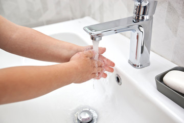 The boy is washing his hands with soap under the water